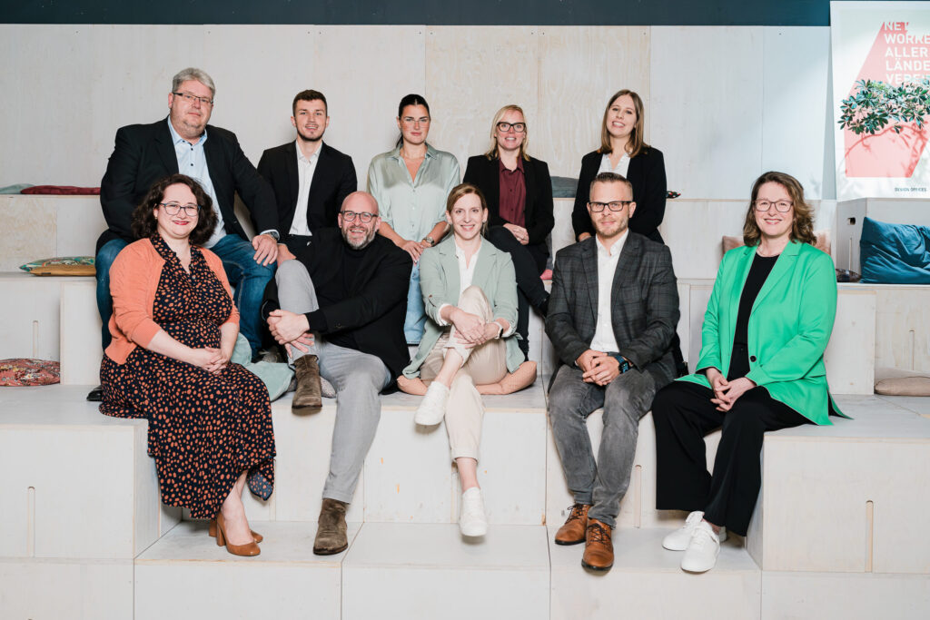 Team-Mitglieder der Abteilung Vergabe sitzen gemeinsam auf einer Treppe und lächeln in die Kamera