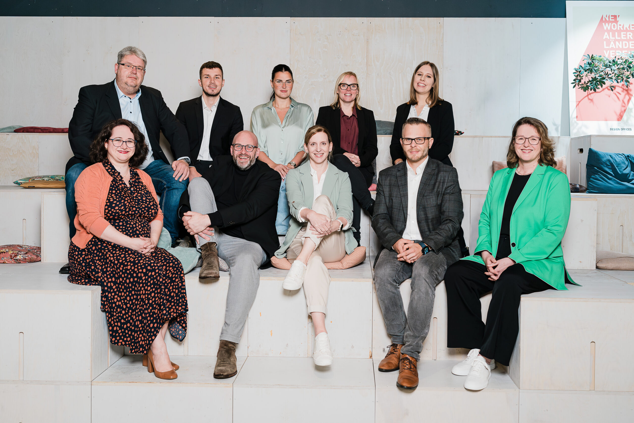 Team-Mitglieder der Abteilung Vergabe sitzen gemeinsam auf einer Treppe und lächeln in die Kamera